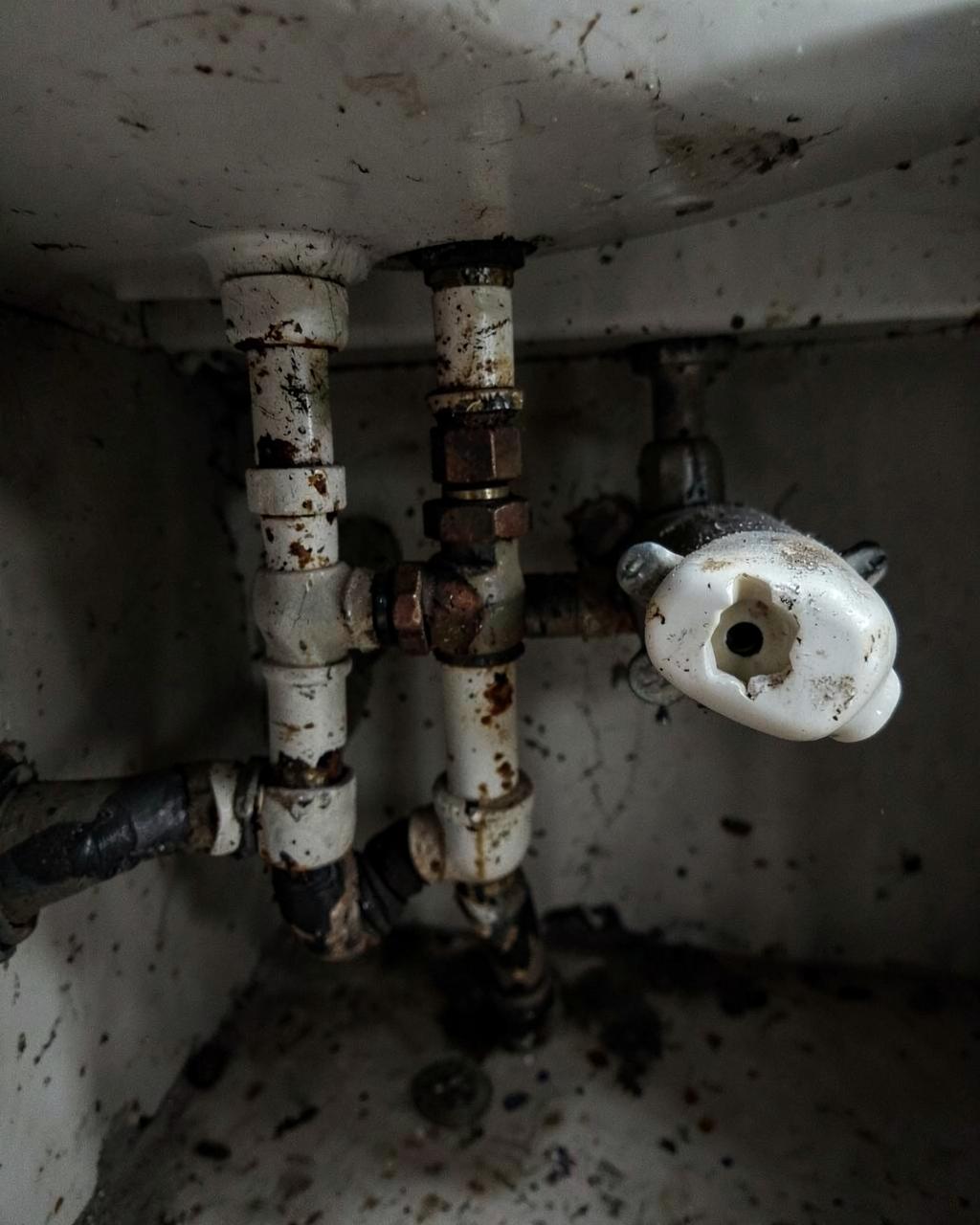 Alte rostige Wasserleitungen und defekte Armatur unter einem Waschbecken
